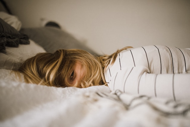 A girl with hair in her face laying on a bed looking tired and exhausted