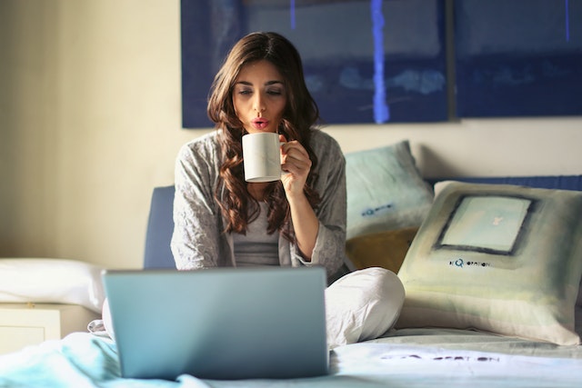 Lady sitting in her bed working on her computer drinking coffee.