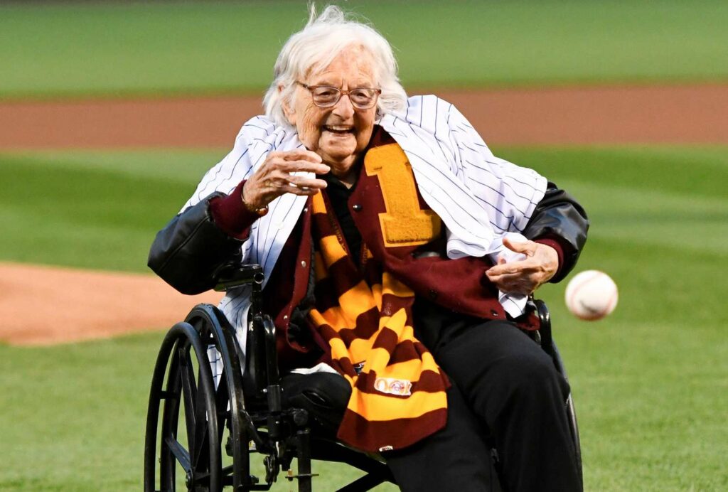 An older woan in a wheel chair on a baseball field throwing out a pitch