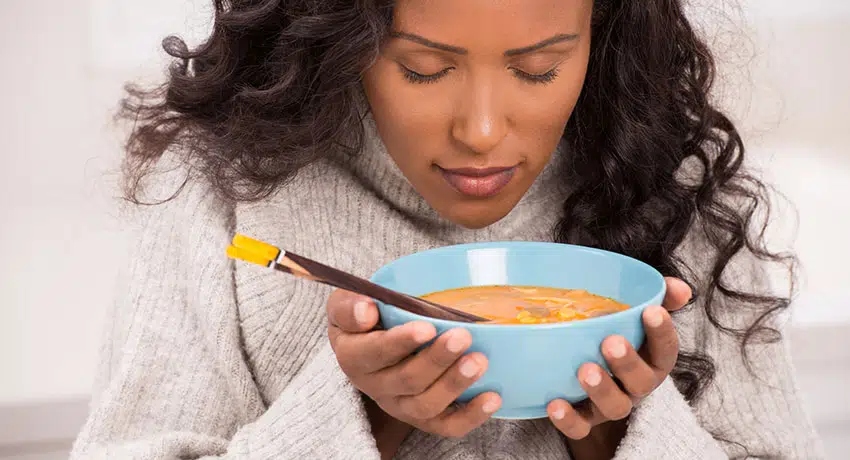 Woman enjoying a bowl of soup wearing a sweater